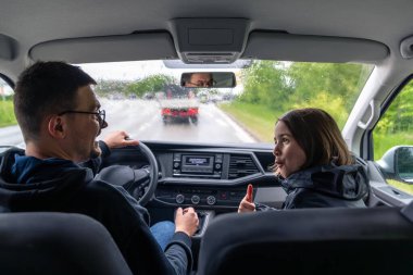 Yağmurlu havada araba süren bir adam ön koltuktaki kız sevinçle onay verirken. Aracın içinden yağmurlu bir havayla vurulmuş..