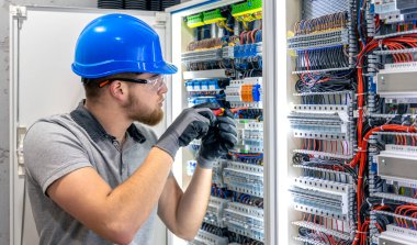 Santralde çalışan üniformalı bir erkek elektrikçi. Elektrik var. Yüksek kalite fotoğraf. Sert şapkalı erkek elektrikçi. Erkek bir elektrikçi elektrikle ilgili bir sorunu çözer.