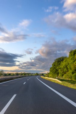 Gürültü bariyerleri ve manzaralı günbatımı gökyüzü olan boş bir karayolu köprüsü manzarası.
