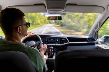 Açık bir bahar gününde bir adam düz bir kırsal yolda araba sürer. Odaklanmış bakışları direksiyonun arkasındaki sorumluluğu ve kontrolü yansıtıyor..