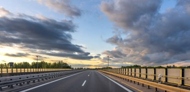 Parlayan günbatımı gökyüzünün altında, uzak bir ufka doğru uzanan boş bir yolu olan huzurlu bir manzara..