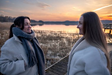 Gezinti güvertesi boyunca yürü. Deniz kenarında bir yürüyüş. Doğada yürümek. Gün batımı. Yüksek kalite fotoğraf. Sur boyunca yürüyen iki kadın. Soğuk hava.