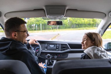 Bir adam yolcu koltuğunda bir kızla araba sürerken gülümsüyor. Parlak sabah ışığı ve taze yeşil dışarıdaki sıcak ve keyifli aile yolculuğunu iletir..