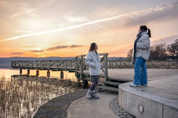 Gezinti güvertesi boyunca yürü. Deniz kenarında bir yürüyüş. Doğada yürümek. Gün batımı. Yüksek kalite fotoğraf. Sur boyunca yürüyen iki kadın. Soğuk hava.