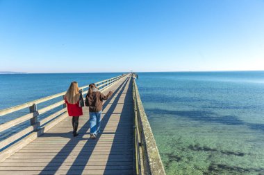İskelede iki kadın. İskelede yürüyen iki kadının arka görüntüsü. Yüksek kalite fotoğraf. Deniz. Mesaj için yer var. Gezinti güvertesinde yürü.