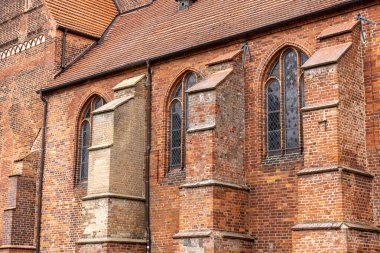Gotik kemerli pencereler, kırmızı duvar payandaları ve manevi mirası çağrıştıran ortaçağ mimarisinin yer aldığı tarihi tuğla kilisenin yan görüntüsü.
