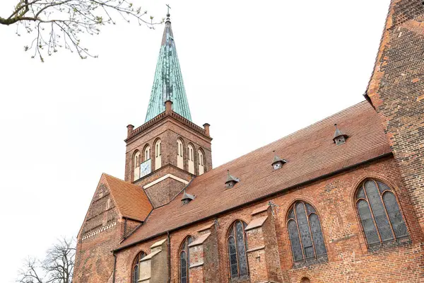 Uzun yeşil kulesi ve kırmızı tuğlalı gotik cephesi olan tarihi bir kilise, kemerli camları ve Avrupa mimarisi tarzında bir saat kulesi var..