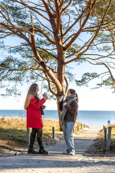 Deniz kıyısındaki termostan sıcak kahve içen iki kadın. Doğa. Deniz. Rıhtım. Yüksek kalite fotoğraf. Soğuk hava, bahar, sonbahar.