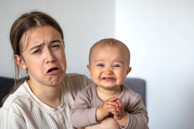 Bir bebek ve bir genç, evde birlikte aptalca suratlar yapıyor, sıcak bir ev ortamında neşeli ve komik bir etkileşim yakalıyorlar..