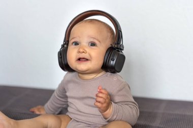 Bej tulumlu bir bebek büyük kulaklıklı bir yatakta oturuyor, şaşırmış ve büyülenmiş görünüyor..