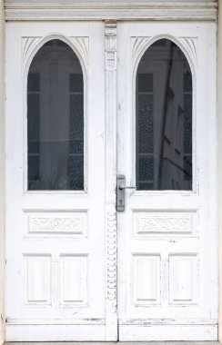 Eski beyaz ahşap kapı, vitraylı camlar ve kemer desenli. Klasik alçılı bina cephesinin bir parçası..