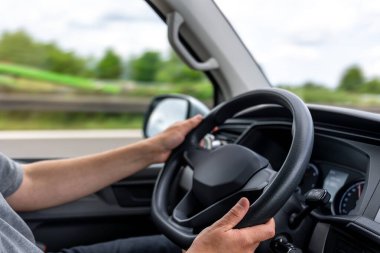 Araba kullanırken direksiyondaki ellerin yakın görüntüsü. İç görünüm denetimi ve güvenli sürüş odağı vurguluyor.