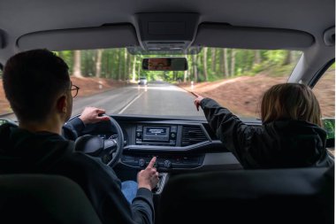 Sürücü yağmurlu yola odaklanırken gri başlıklı bir kız ön koltukta oturur ve önüne bakar. Samimi ve içten bir an..