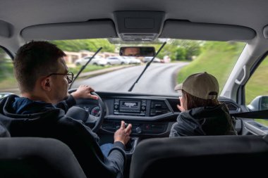 Yağmurlu havada, cam silecekleri açık bir şekilde kırsal bir yolda araba süren bir adam var. Yeşil manzara ve dışarıdaki ıslak koşullar.