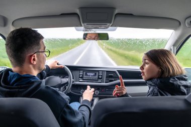 Ön koltuktaki kız yağmurlu bir yolculuk sırasında şoförle konuşurken esprili bir şekilde hareket eder. Sıcak ve neşeli bir yolculuk anı.