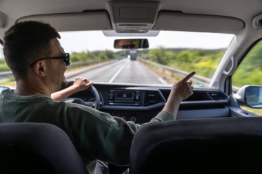 Yolculuk sırasında köprüde araba süren bir adam. İçeriden çekilen sürücü güneşli bir günde ileriyi işaret ediyor..