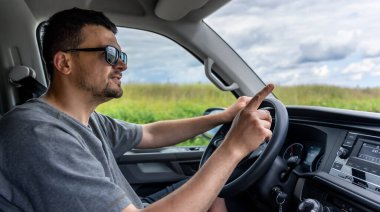 Adam araba sürerken parmaklarıyla hareket eder, önündeki yola odaklanır. Güçlü sürüş gücüyle sakin gün ışığı sahnesi.
