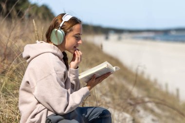 Deniz kıyısında kitap okuyan genç bir kız. Deniz kıyısında müzik dinleyen bir kız. Yüksek kalite fotoğraf. Deniz kıyısında meditasyon. Metin için boşluk.