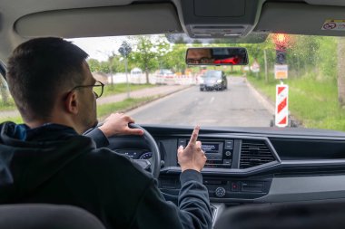 Siyah kapüşonlu bir adam yağmurda araba sürüyor, ıslak camın arkasındaki trafik lambasında bekliyor..