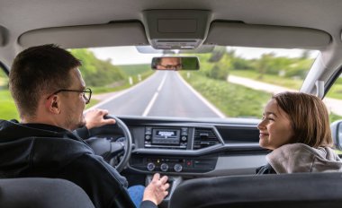 Ön koltukta oturan bir kız, araba boş bir bahar yolunda ilerlerken sürücüye gülümsüyor. Dışarısı aydınlık ve sakin. Huzurlu bir yolculuk hissi uyandırıyor..