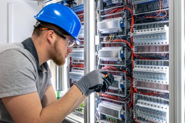 Koruyucu teçhizatlı bir adam santralin içindeki kabloları elle bağlar. Teknik ayar, yapay ışık ve hassas profesyonel eylem..