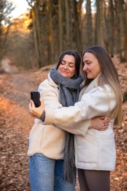 Ormanda telefonlarıyla selfie çeken iki arkadaş. Doğadaki arkadaşlar. Yüksek kalite fotoğraf. İlkbahar, sonbahar mevsimi. Ormanda bir yürüyüş, doğada..