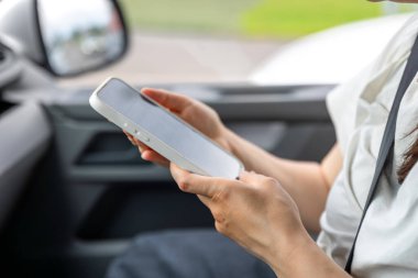 Arabada elinde akıllı bir telefonla oturan ve yolculuk sırasında ekranla etkileşime giren bir kadın yolcu. Günışığı ve modern arabanın içi görünür..