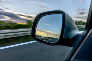 Rüzgar türbinleri gün batımında hareket halindeki bir arabanın yan aynasına yansıyor..