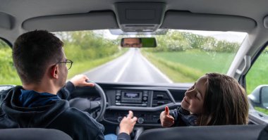 Ön koltukta bir kız ona doğru dönerken arabayı süren adam. Yağmurlu bir yol ve samimi, bağlantılı bir seyahat anı.