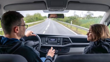 Yağmurlu bir araba yolculuğu sırasında ön koltuktaki bir kız gülümsüyor. Islak ön cam ve neşeli ifade sıcak bir yolculuk anı yaratır..