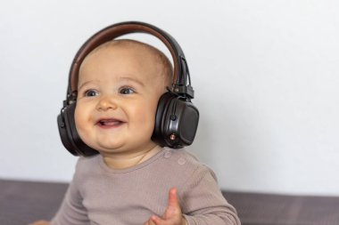 Yan bakarken büyük kulaklıklarla gülümseyen neşeli bir bebek. Görüntü, duyguyu, sıcaklığı ve sesle neşeli bağı yakalar..
