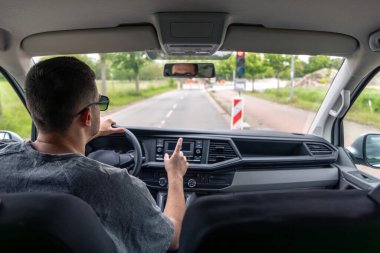 Araba bir şehir caddesinde kırmızı ışıkta durdu. Sürücü trafik ışığı ve engeller görünürken bekliyor.