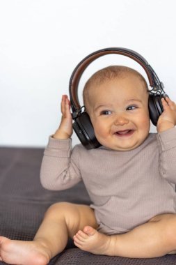 Yatakta büyük kulaklıklarla oturan mutlu bebek, ışıl ışıl gülümsüyor. Duygu ve masumiyetle dolu neşeli ve sıcak bir ev sahnesi..