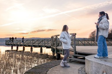 Gezinti güvertesi boyunca yürü. Deniz kenarında bir yürüyüş. Doğada yürümek. Gün batımı. Yüksek kalite fotoğraf. Sur boyunca yürüyen iki kadın. Soğuk hava.