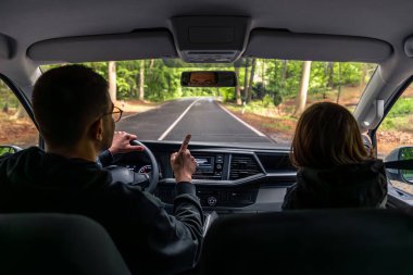 Kapüşonlu bir kız sakince ön koltukta oturur ve ilerideki yağmurlu yolu seyreder. İç görünüş sessiz ve seyahat havası yaratır..