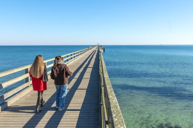 İskelede iki kadın. İskelede yürüyen iki kadının arka görüntüsü. Yüksek kalite fotoğraf. Deniz. Mesaj için yer var. Gezinti güvertesinde yürü.