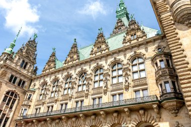 Klasik taş oymaları ve mavi gökyüzüne karşı döşenmiş yeşil çatılarla süslü tarihi bir bina. Avrupa mimari mirasının çarpıcı bir örneği.