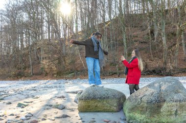 Sahilde kayanın yanında yürüyen mutlu arkadaşlar. İki tane buzlu kadın. Yüksek kalite fotoğraf. Deniz kenarında bir yürüyüş, soğuk hava. Açık havada..