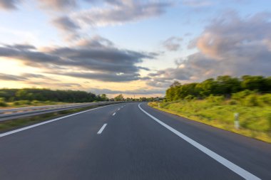 Gün batımında hareket bulanıklığıyla manzaralı kırsal kesimden geçen uzun ve boş bir yol..