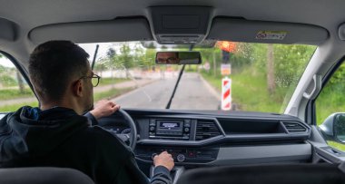 Araba yağmurlu koşullarda sürer. Ön cama yağmur damlaları ve hareket halindeki silecekler..