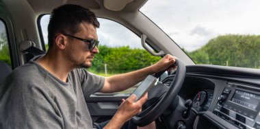 Arabanın içindeki adam araba sürerken dikkatle akıllı telefon ekranına bakar. Çekim içeriyi yakalar ve hareket halinde odaklanır..