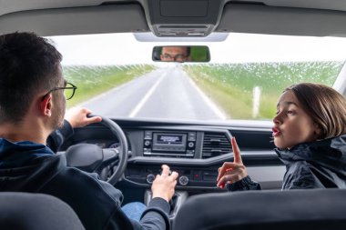 Ön koltuktaki kız, yağmurlu bir yolculukta başparmağını kaldırıyor ve sürücüye gülümsüyor. Neşeli ve konuşkan bir an..