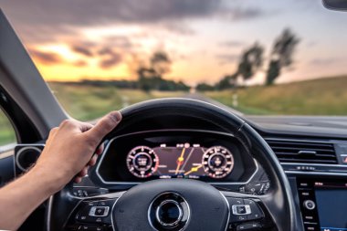 Direksiyona yakın plan, ön camında da yol bulanıklığı var. Günbatımı tonları ve hareketleri seyahat enerjisi ve odaklanma iletir.