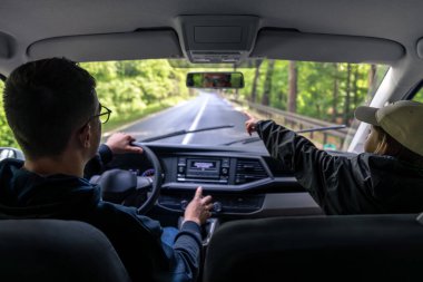 Şoför yağmurlu havada direksiyon sallarken kapüşonlu genç bir yolcu sakince ileriye bakıyor. Huysuz araba zamanı..