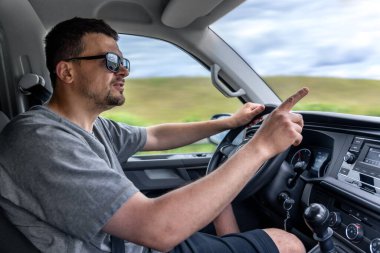 Güneş gözlüklü bir adam araba sürerken işaret parmağıyla hareket eder. Etkileyici iletişim ve gerçek sürüş anına odaklan..