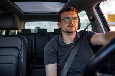 Günbatımında modern bir araba kullanan, emniyet kemeri takan, yola odaklanmış, panoramik sunroof 'lu iç mekan manzaralı bir adam..