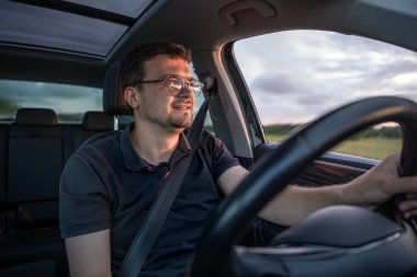 Sıcak gün batımı ışığıyla aydınlatılmış bir araba süren gülümseyen bir adam. Görüntü, modern yaşam tarzında rahatlık, hareket ve pozitiflik yayıyor..