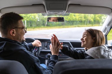 Bir kız ve bir adam arabada avuçlarına dokunuyor, birbirlerine içtenlikle gülümsüyorlar. Güneşli bahar aile gezisinde neşeli bir bağ ve güven jesti..