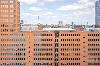 Birçok penceresi olan simetrik tuğla bina cephesi, kuleleri ve haberleşme kuleleri olan bir şehir siluetine karşı kurulmuş. Dengeli ve yapılandırılmış şehir tasarımı.