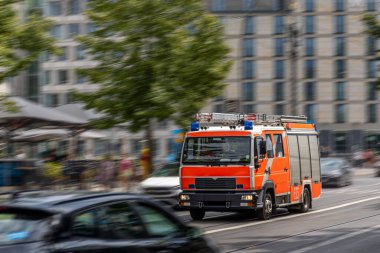 Parlak turuncu bir itfaiye aracı şehir yolunda hızla ilerliyor. Sahnenin hareket bulanıklığı ve aciliyeti acil durum tepkisinin özünü yakalıyor..
